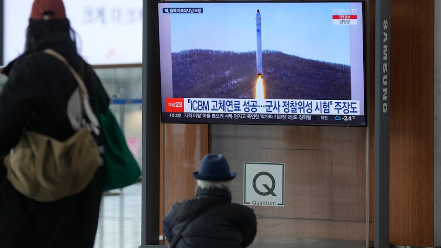 two people watch a tv screen showing a North Korean missile test