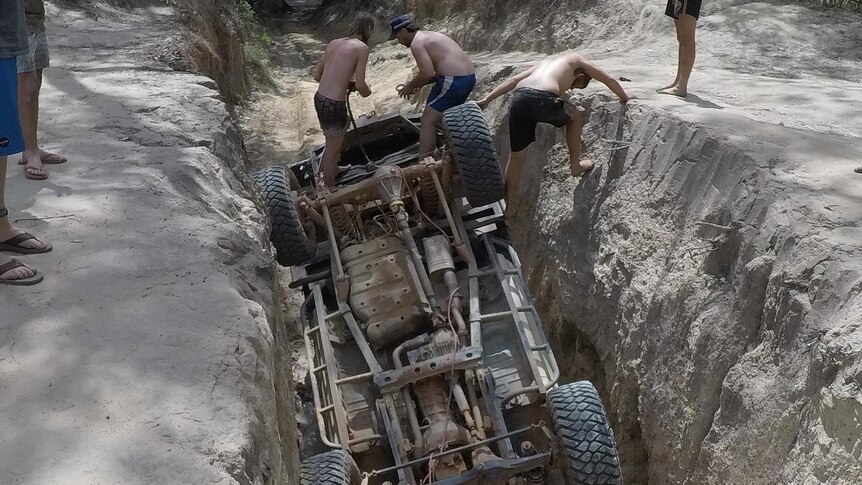 Photo of overturned car in a deep rut with people standing around it