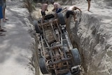 Photo of overturned car in a deep rut with people standing around it
