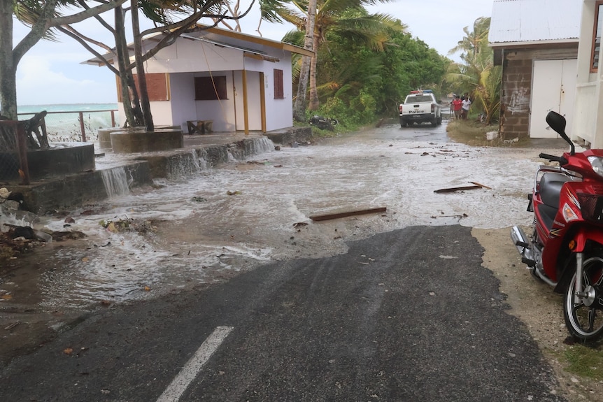 Seawater spills onto the road in Funafuti, Tuvalu during a king tide, as a car travels down the road.