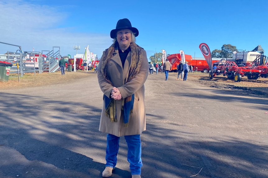 A woman in a black hat and brown coat stands outside.