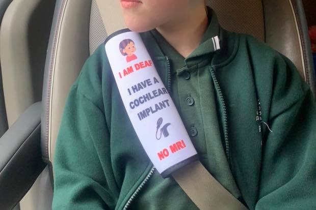 A girl sits in a car seat looking out the window with a seat belt cover with medical information attached to her seat belt.