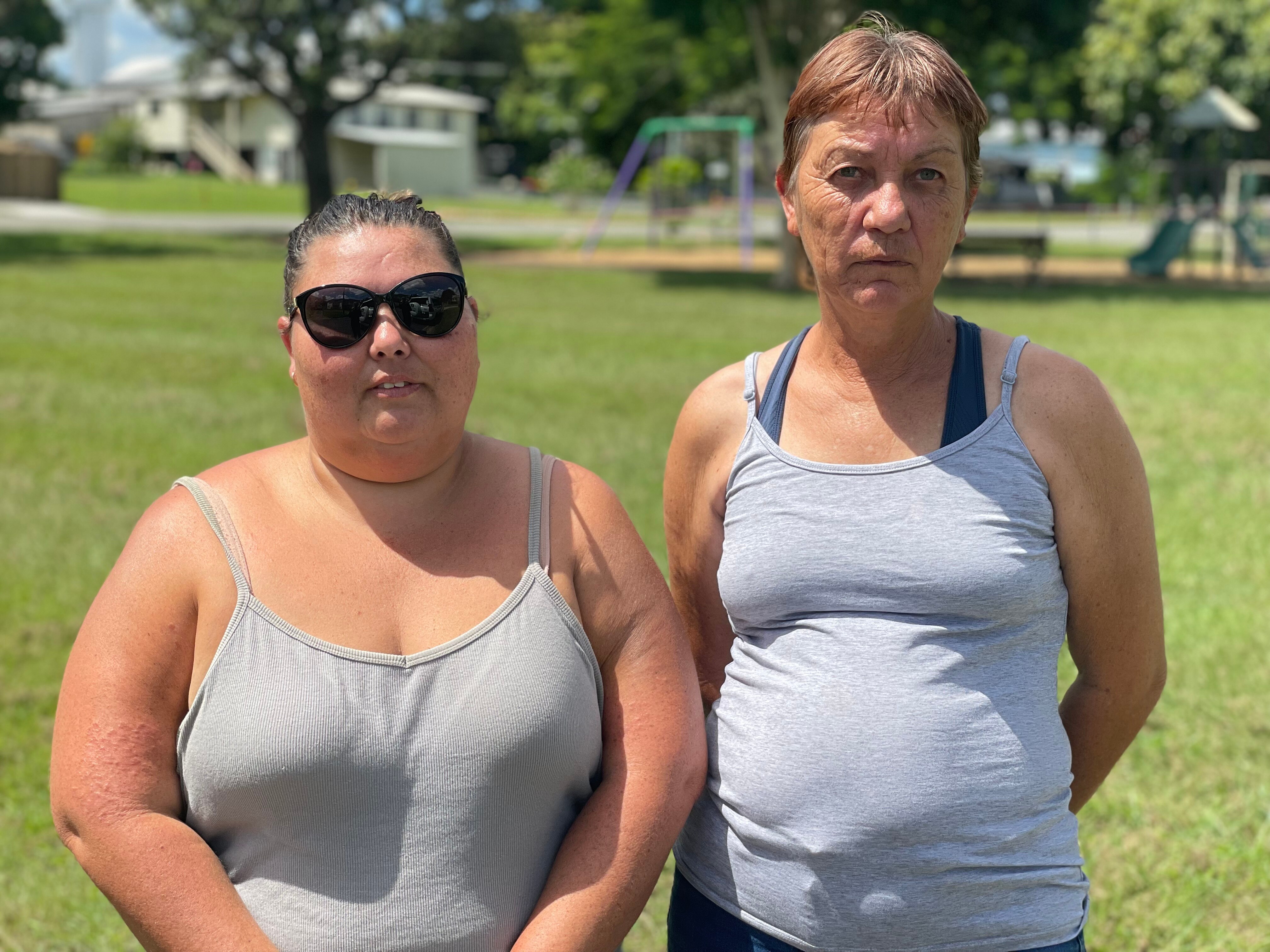Two woman stand in park, serious expressions