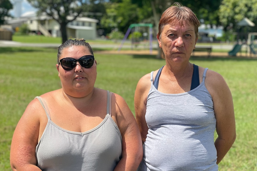 Two woman stand in park, serious expressions