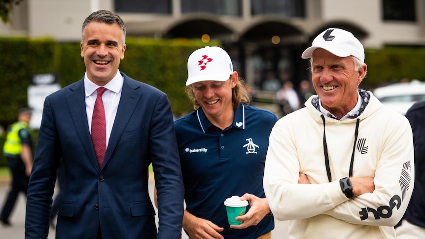 Three men smiling and walking, two of them in sportswear and one in a business suit