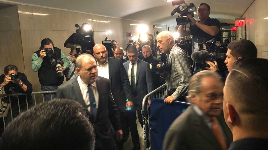 Harvey Weinstein walks through a media pack in a line of men in suits