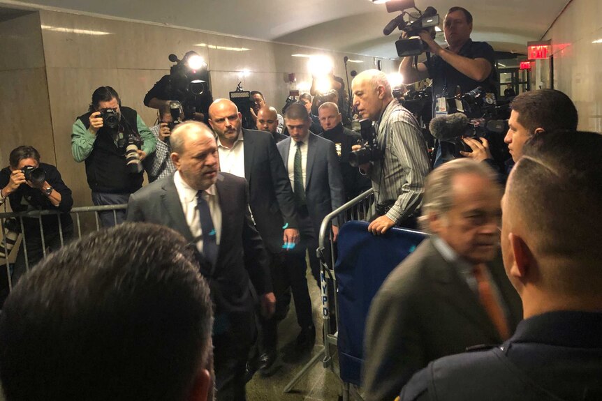 Harvey Weinstein walks through a media pack in a line of men in suits