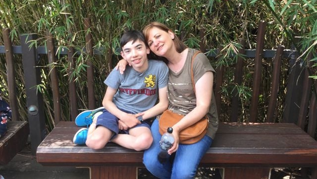 David Tankey and his mother Molly sit on a wooden bench and smile at the camera.