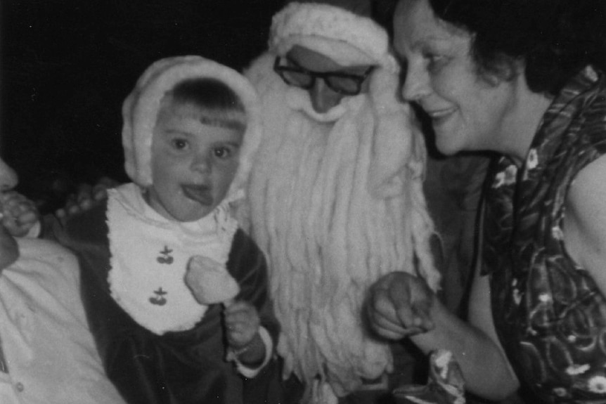 a black and white photo of santa and a kid smiling at the camera