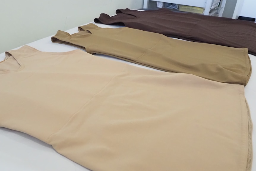 Three singlet-shaped binders made with fabrics of different skin tones lie on a medical bench