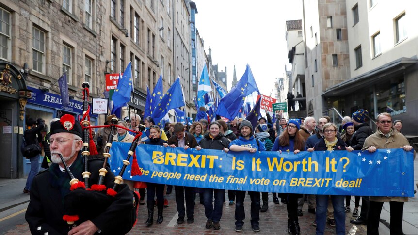 A piper leads a group of protesters who are holding a banner with the word Brexit is it worth it on it
