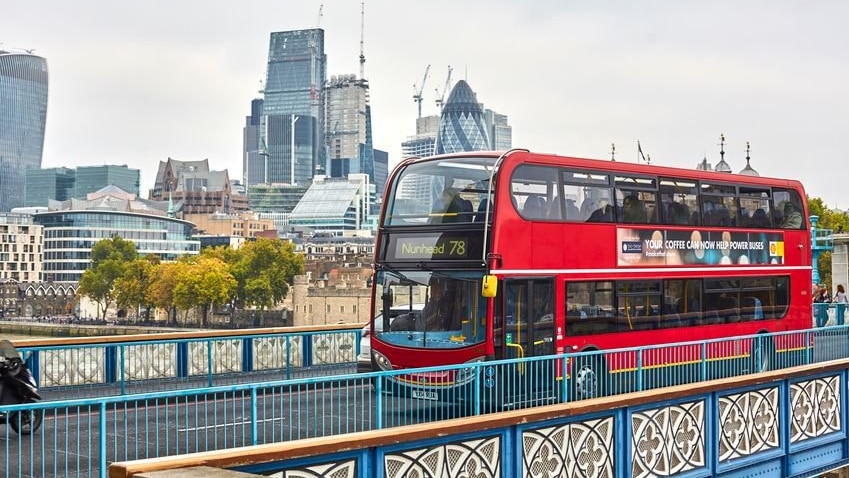 A London bus drives across the bridge with a sign saying "powered by coffee beans".