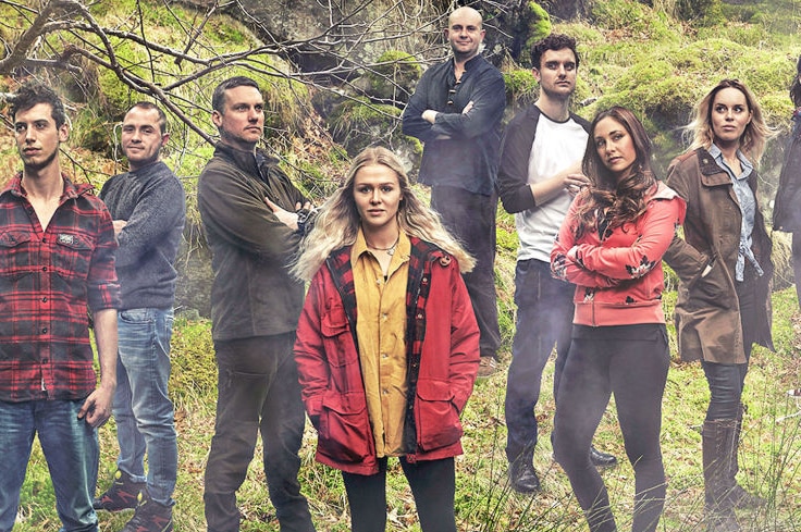 A group of men and women stand among trees in a forest