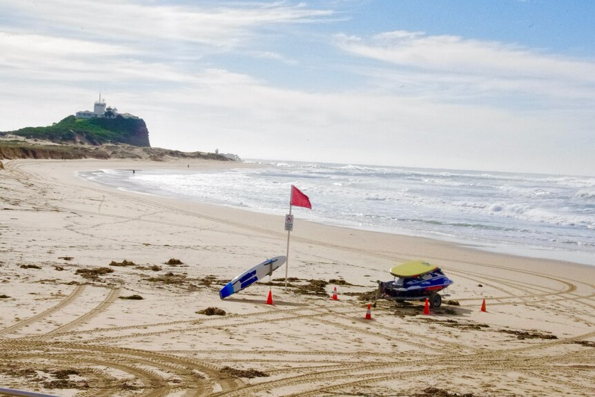A red flag and surf rescue equipment on a deserted shoreline at Nobby's beach in Newcastle.