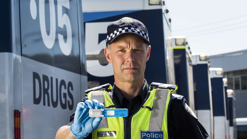 A police officer wearing high vis vest and a glove holds up a drug testing device