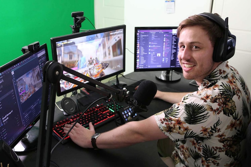 Alex Hockings sits in his 'office' complete with lights, cameras, three gaming computers and a floor-to-ceiling greenscreen.
