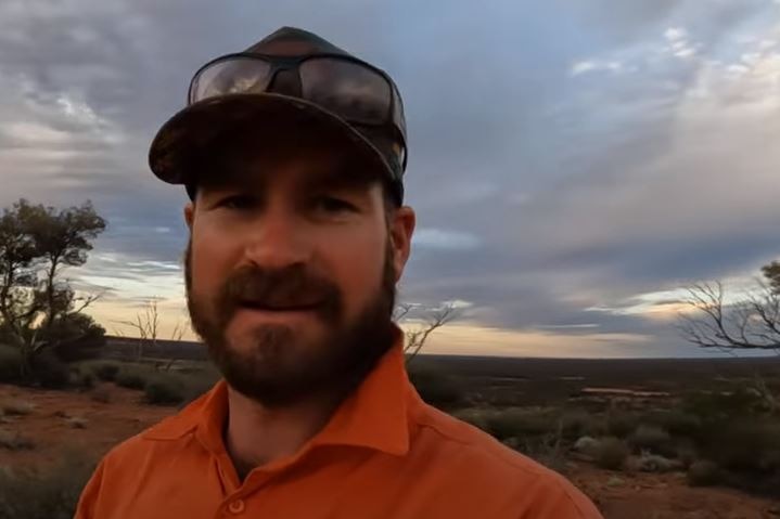 A man with a trim beard in a cap and collared shirt.