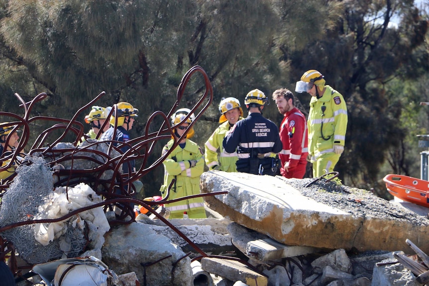 Firefighters and search and rescue personnel gather behind a twisted mound of building debris.