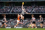 Collingwood's Mason Cox leaps high and takes the ball in one hand at a contest as players stand around.