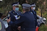 Two police officers wearing face masks shake hands at a piping out.