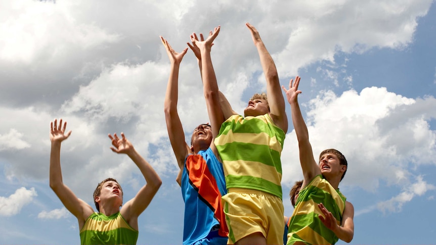 Four teenage boys leaping into the air as if to catch a ball, wearing sports jerseys.