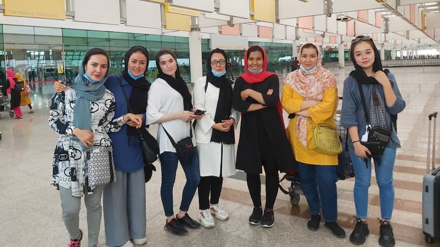 Seven women standing side by side at the airport