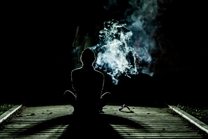 Silhouetted person with illuminated cloud of smoke.