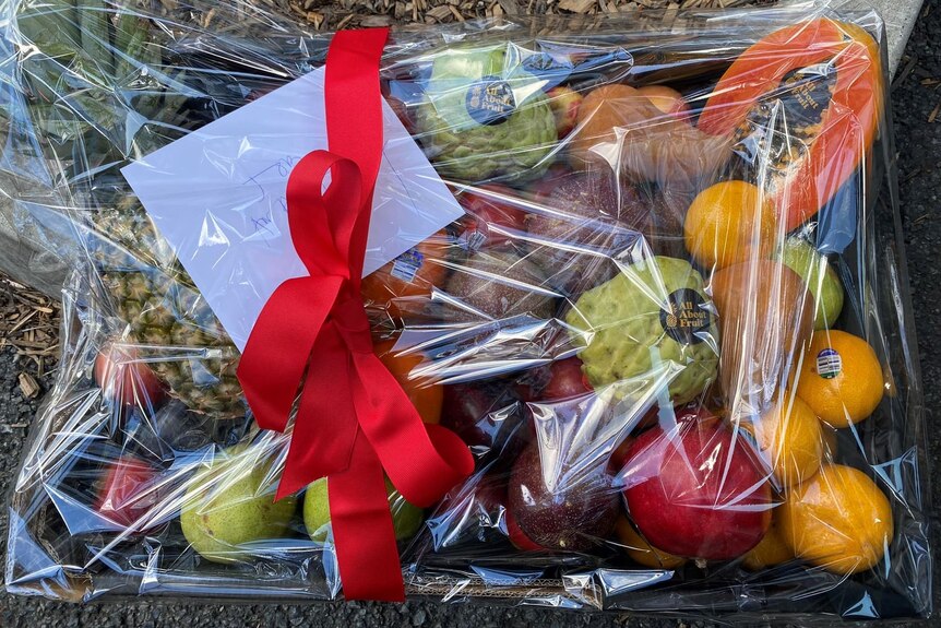 A colourful basket of fruit wrapped in a red bow with a card