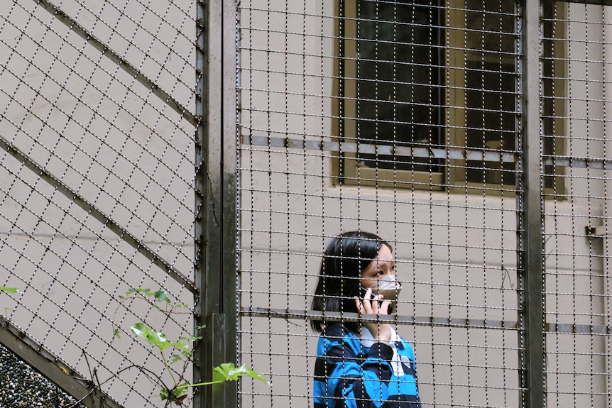 Kewen stands on the phone behind the fence in her apartment building
