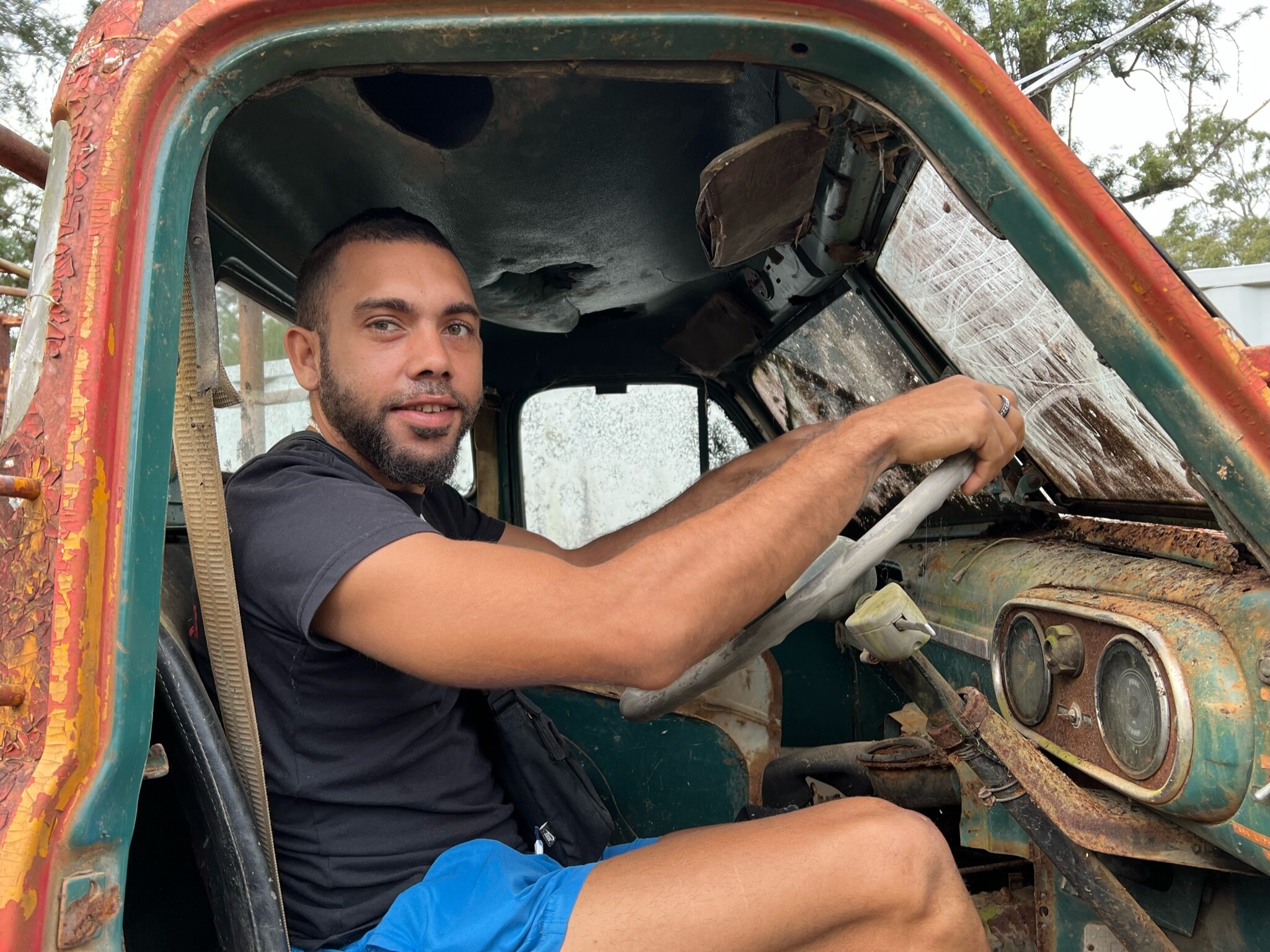 A young Indigenous man sits behind the wheel of an old rusty fire truck.