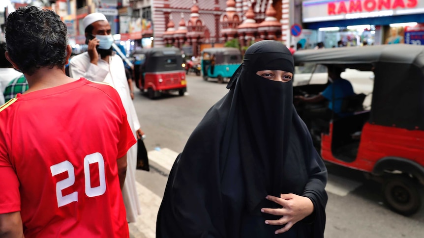 A woman walks down a busy road while wearing a black burqa with only her eyes visable.