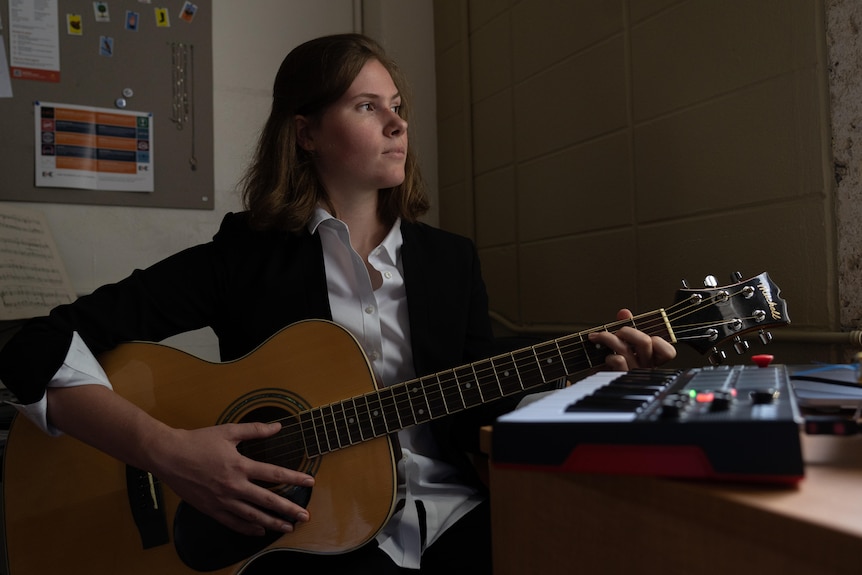 Woman playing a guitar and looking out her window. 