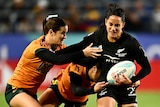 A New Zealand women's rugby sevens player runs with the ball as she is tackled by two Australian players.