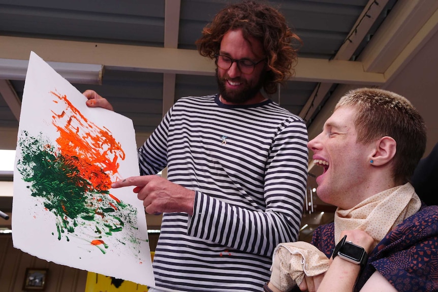A man holding art work and a man in a wheelchair smiling