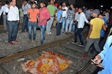 An orange and yellow blanket covers a body on train tracks in India.