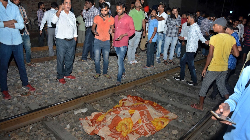 An orange and yellow blanket covers a body on train tracks in India.
