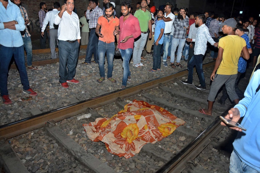 An orange and yellow blanket covers a body on train tracks in India.