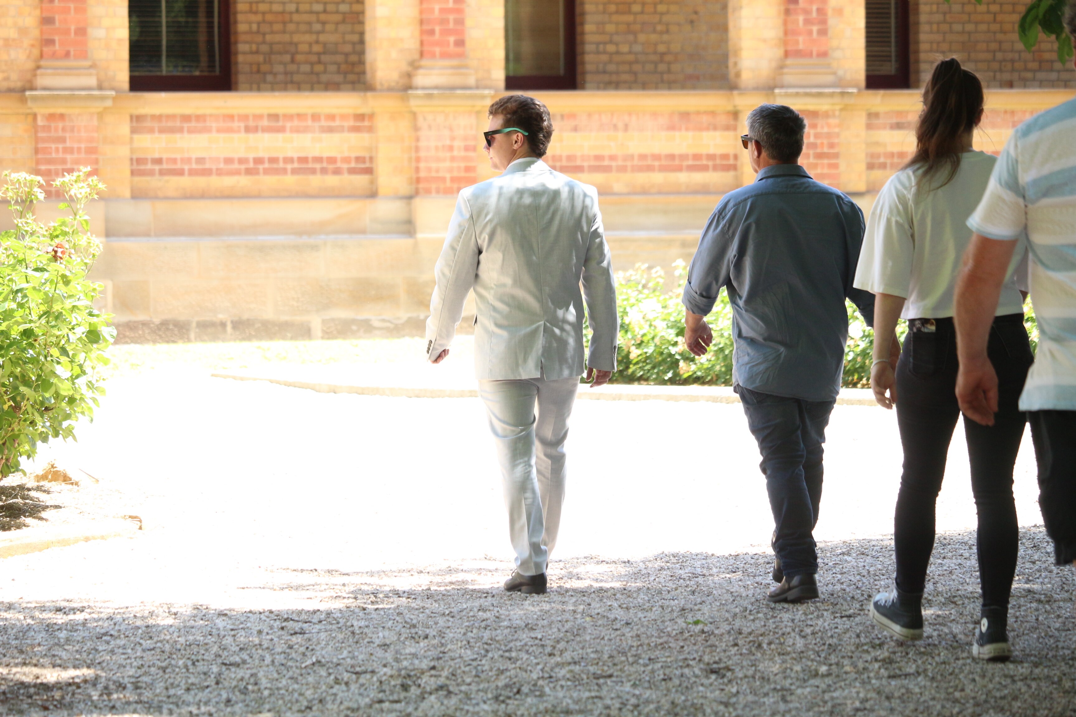 Un hombre con pelo corto y rubio, gafas de sol y un traje color crema entra a un juzgado.