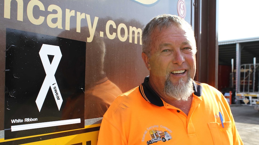 Truck driver standing in front of truck with a stick with a white ribbon on it.