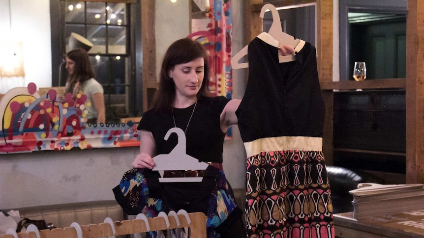 A woman holds up a dress at a clothes swap event