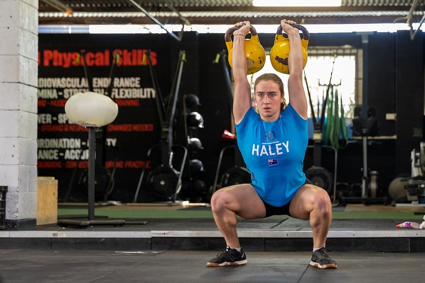Courtney Haley lifting two kettle bells in a squat position.