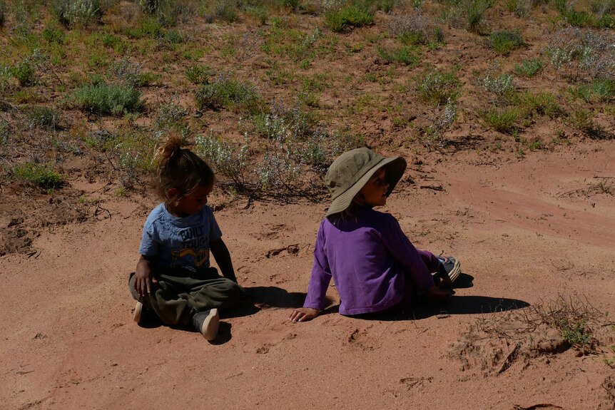 Two children sit on the ground unaware of their surrounding.