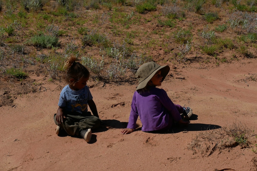 Two children sit on the ground unaware of their surrounding.