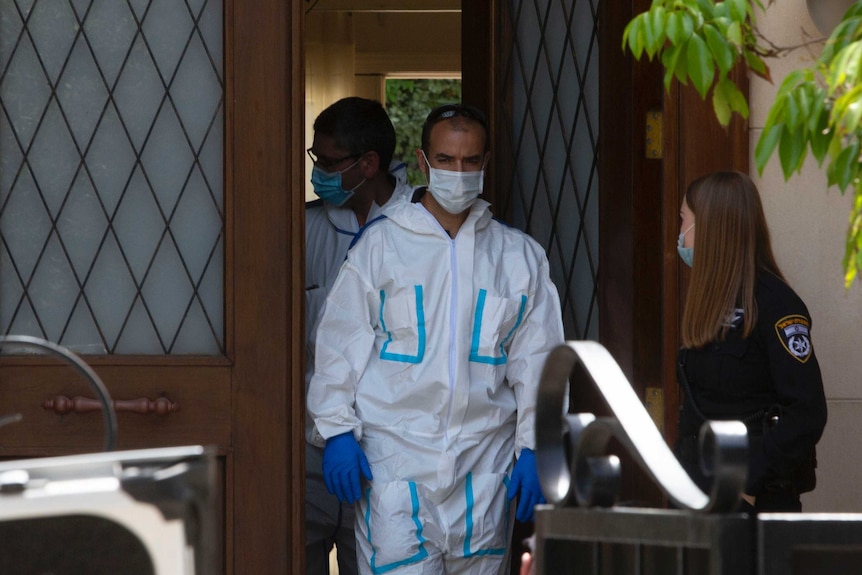 An officer in a hazmat suit exits the front door of a house