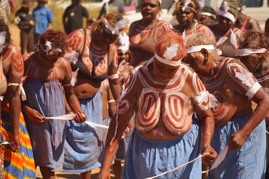Women painted with body markings dance in a ceremony.