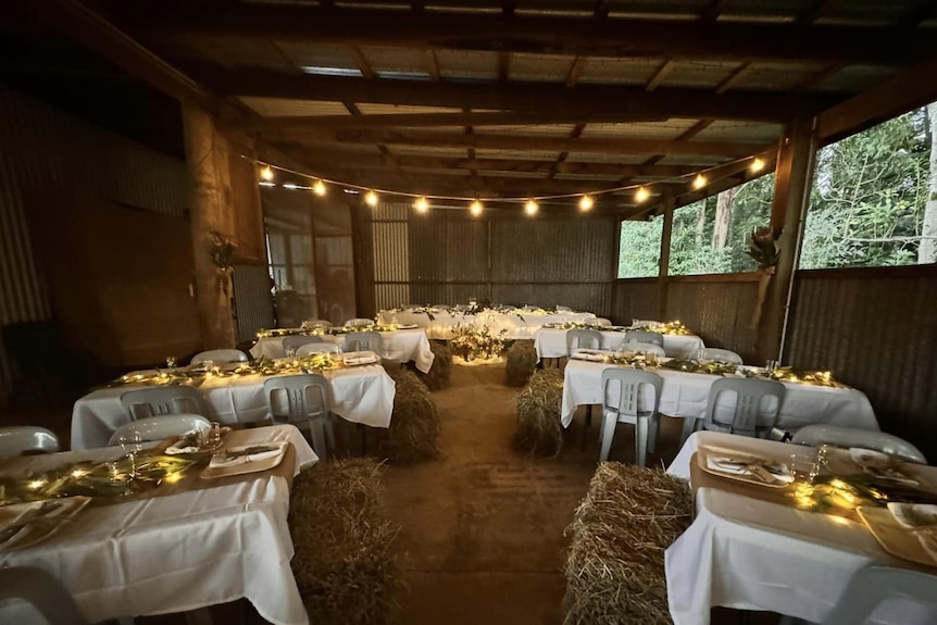 Hay bales and tables in a farm shed with mood lighting.