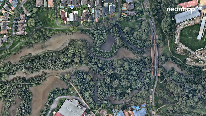 A birds eye view of a flooded creek surronded by trees and houses.
