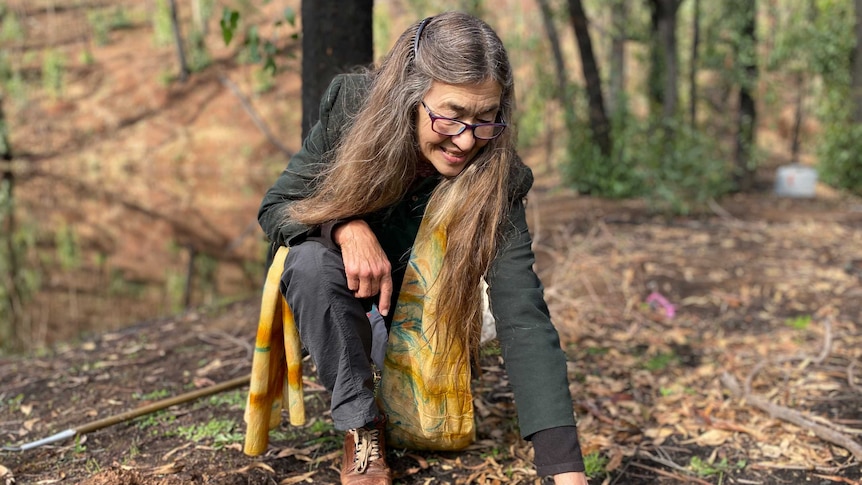 A woman kneels in bushland, pointing to the soil.