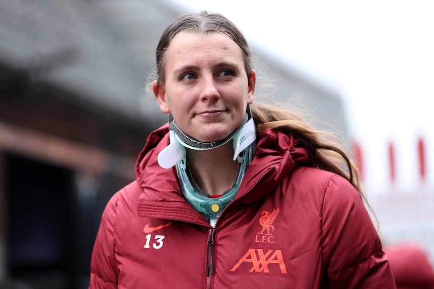 A woman in a red tracksuit with a halo around her neck for support, walking outside