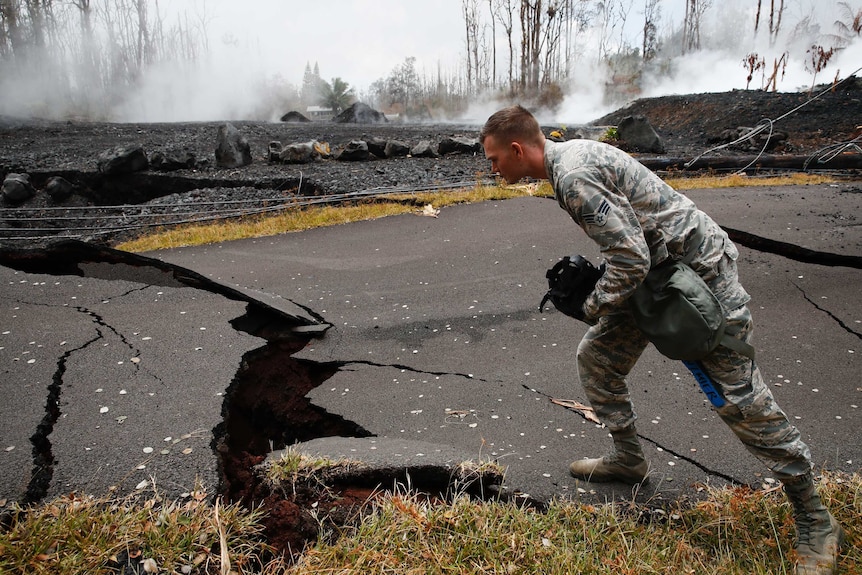 A U.S. Air National Guardsman looks at cracks as toxic gases rise from a crack in the road